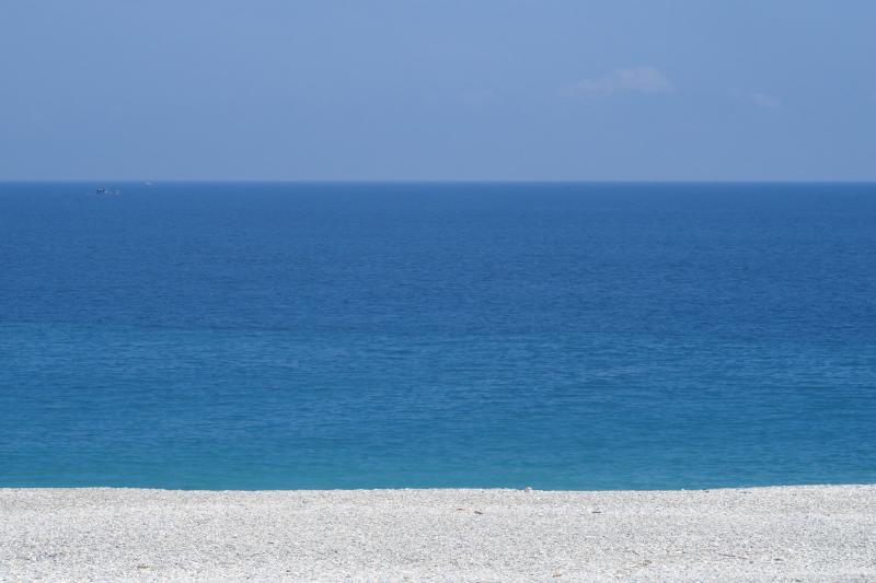 海水在近处是浅蓝，向外逐层加深。远处两只小船，天边一片薄云。